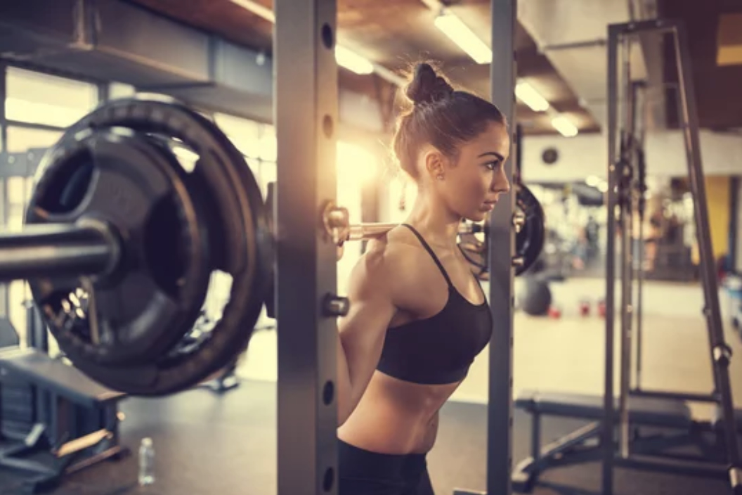 a woman stands in the squat rack ready to squats with heavy weights